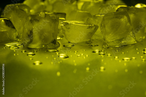 Ice cubes in yellow on a reflecting table with ice drops
