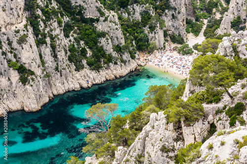 View from above of the calanque of En-Vau, a hard-to-reach narrow natural creek with white sandy beach close to Marseille and Cassis, with people sunbathing and swimming in the crystal clear water.