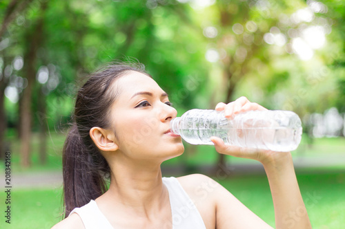 Woman drinking water during a running. Jogging woman in Park. Sunny day. Drinking mode.