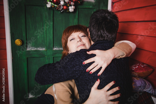 Couple near red wall of small winter home decorated for Christmas and New Year