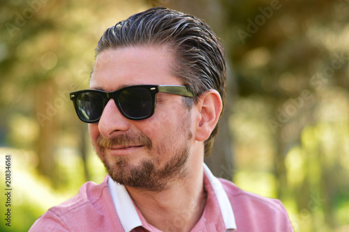 Young man's outdoors portrait looking at the camera who has sunglasses with natural green background. Neutral, happy, sad, disgust, fear, surprise Facial Emotion.