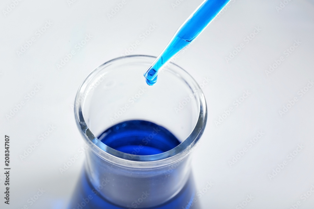 Dripping blue liquid into flask on light background Dripping blue liquid into flask on light background