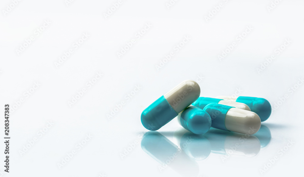 Blue and white capsules pill isolated on white background with shadow and copy space. Global healthcare concept. Antibiotics drug resistance. Antimicrobial capsule pills. Pharmaceutical industry. Blue and white capsules pill isolated on white background with shadow and copy space. Global healthcare concept. Antibiotics drug resistance. Antimicrobial capsule pills. Pharmaceutical industry.