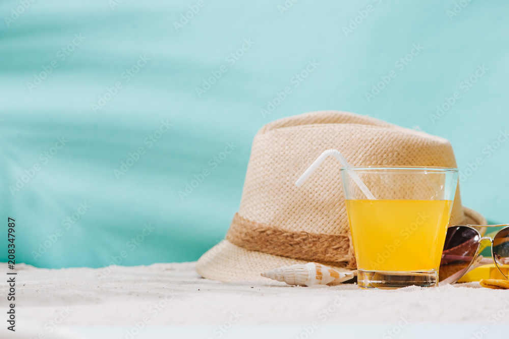 Summer background. Beach accessories flip flops, sunglasses, hat and orange juice on sand background