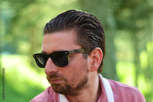 Young man's outdoors portrait looking at the camera who has sunglasses with natural green background. Neutral, happy, sad, disgust, fear, surprise Facial Emotion.