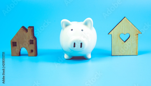 Piggy bank and wooden homes isolated on blue pastel background
