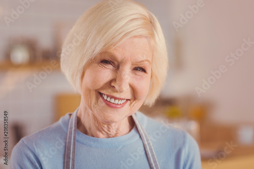 Happy barista. The close up of a cheerful elderly woman in an apron smiling at the camera brightly while working as a barista in a coffee shop