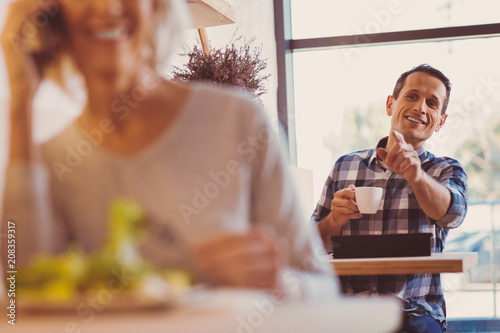 More coffee. The focus being on a pleasant cheerful young man drinking coffee and calling up a waiter, asking for refill while another customer eating salad