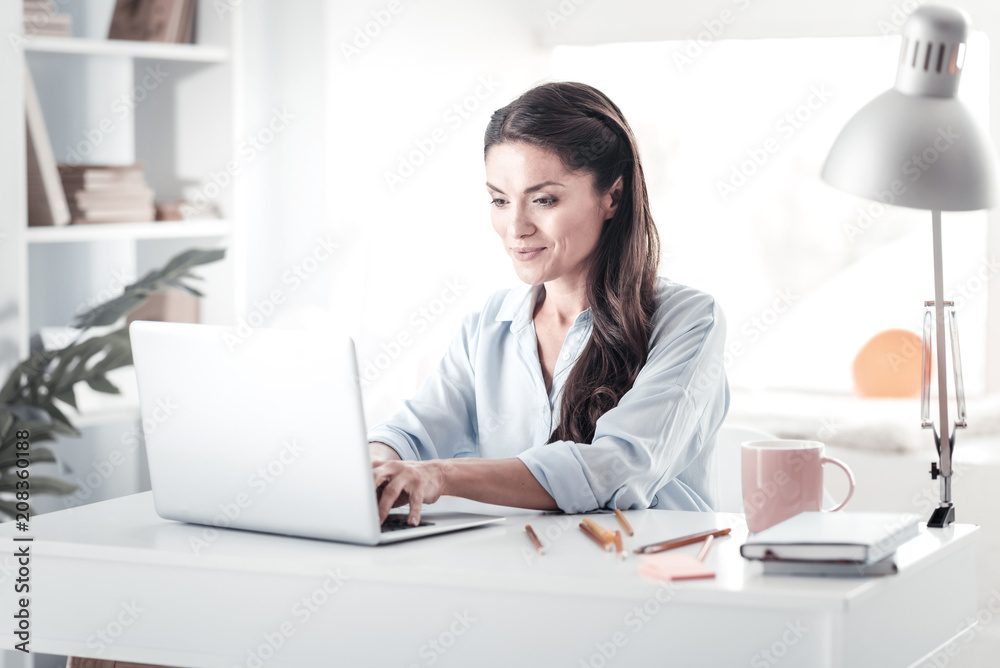 Being busy. Pretty female person expressing positivity while looking at her gadget Being busy. Pretty female person expressing positivity while looking at her gadget
