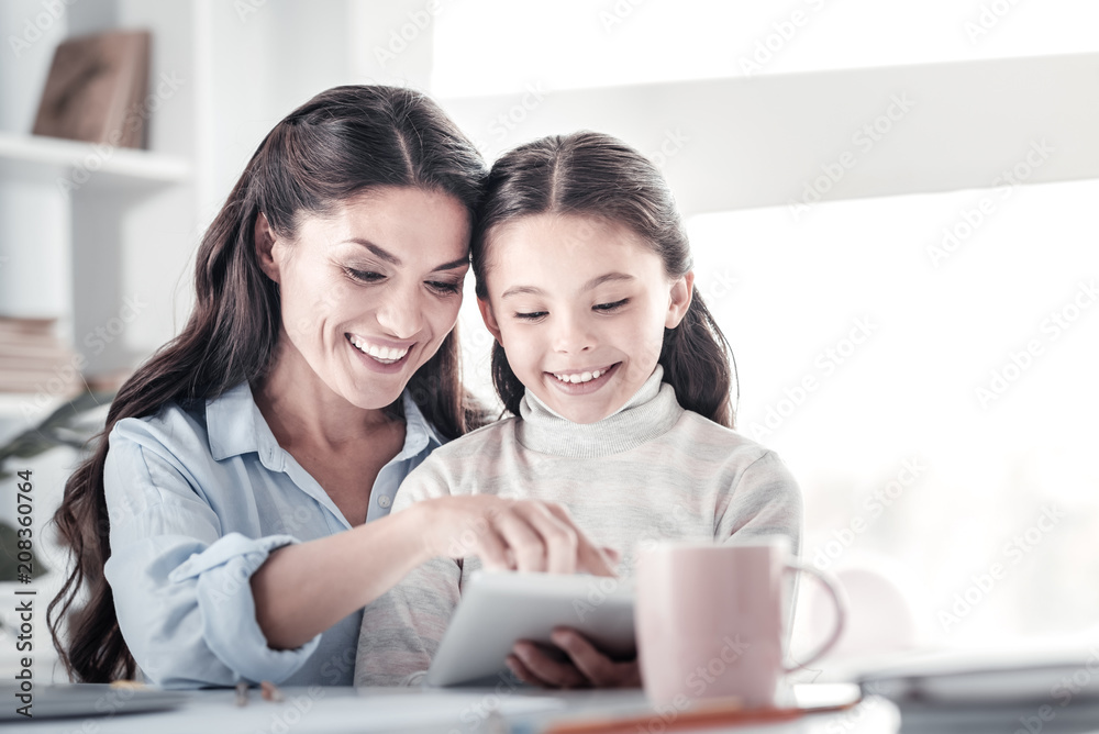 Completing task. Pleased longhaired woman bowing head while embracing her daughter Completing task. Pleased longhaired woman bowing head while embracing her daughter