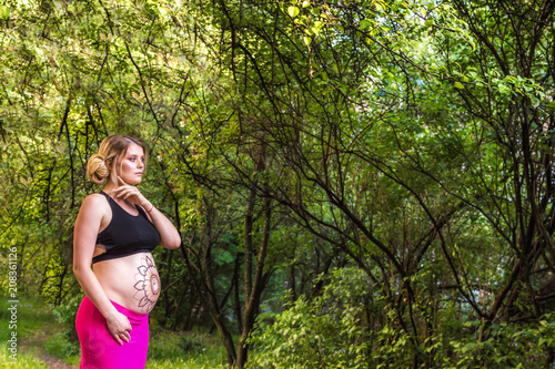 pregnant woman with mehendi on body against the background of green trees. concept photoshoot of pregnancy photo