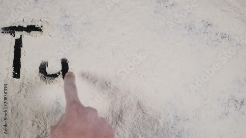 finger write TUESDAY on a white flour background. top view 4k