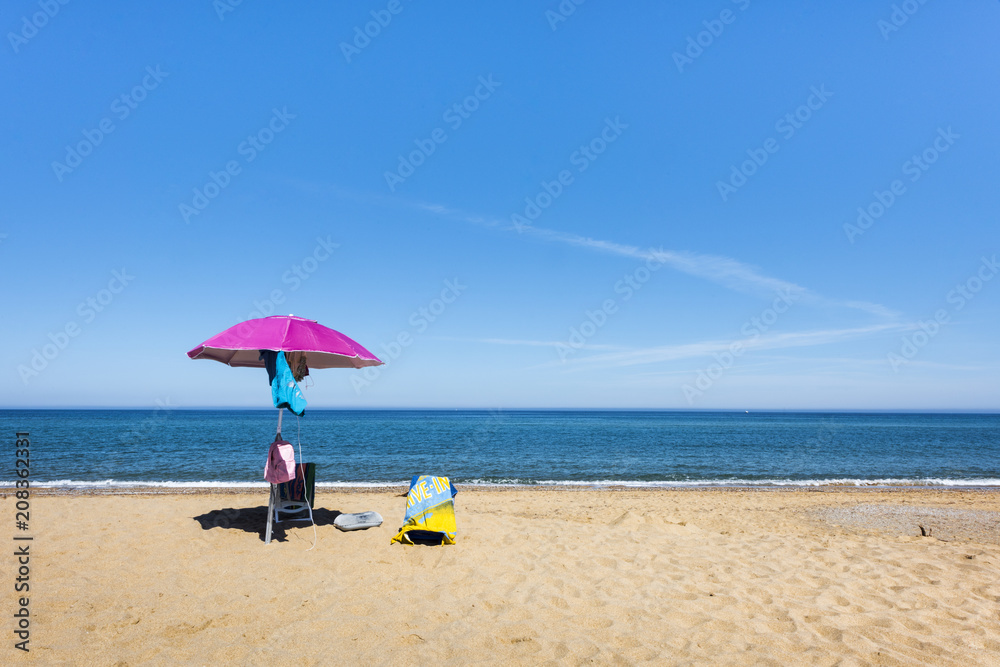 Pink umbrella and deck chairs on the beach in front of the ocean, Sardinia, Italy