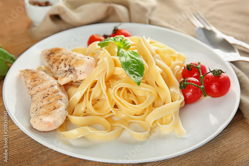 Plate of delicious pasta with grilled chicken fillet and tomatoes on table