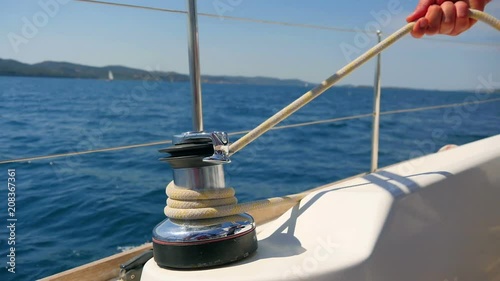 Male hands pulling white rope winded round side winch while making a turn. Filmed on sailing trip in Croatia in slow motion hd.