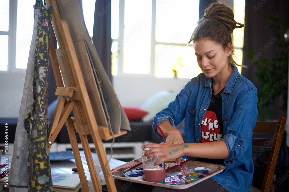 Fototapeta premium Artistic girl sitting in studio and paint on easel.