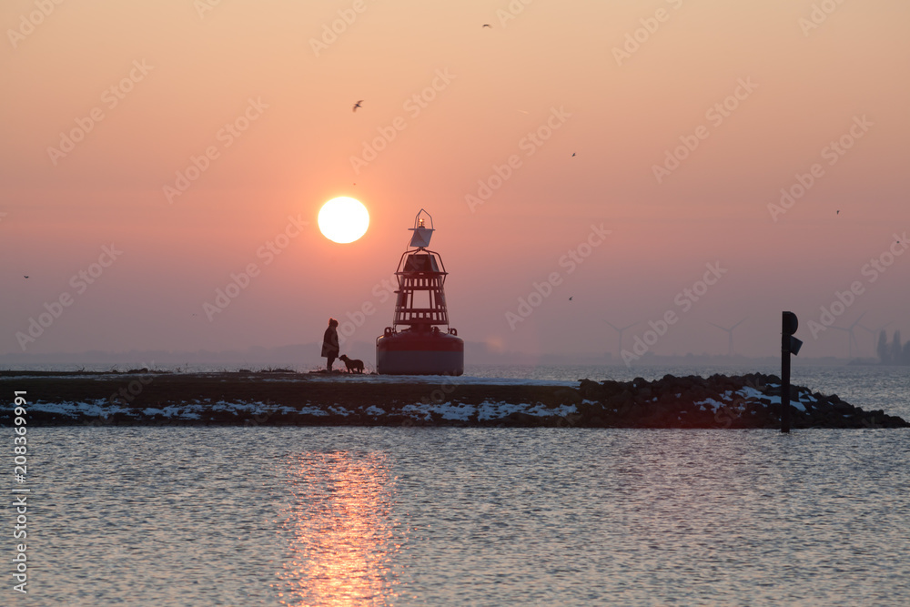 Women walking with dog on pathway to lighthouse at winter sunset