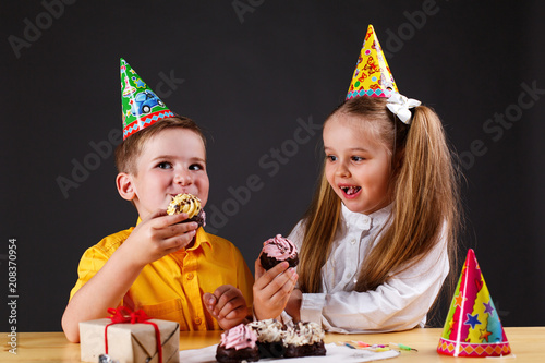 Charming little boy and girl eat a birthday cake sitting at the table in studio photo