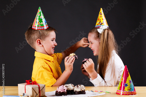 Charming little boy and girl eat a birthday cake sitting at the table in studio photo