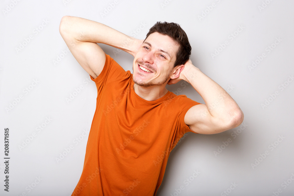 happy young man smiling with hands behind head against gray background happy young man smiling with hands behind head against gray background