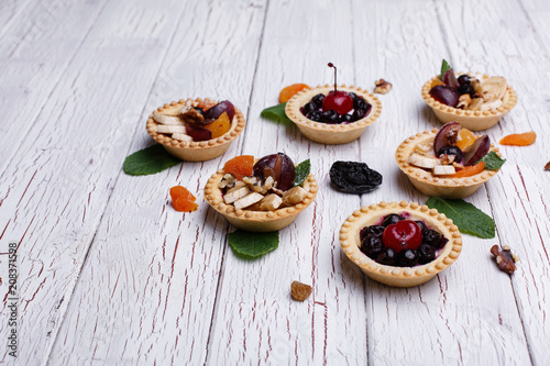 Delicious baked fruit baskets with berries, exotic fruits, greenery and nuts served on white wooden table