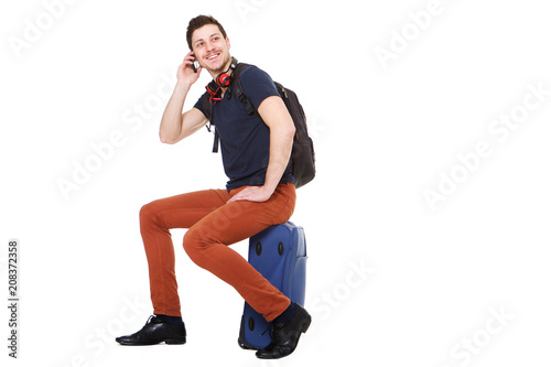 male traveler sitting on suitcase and talking on mobile phone