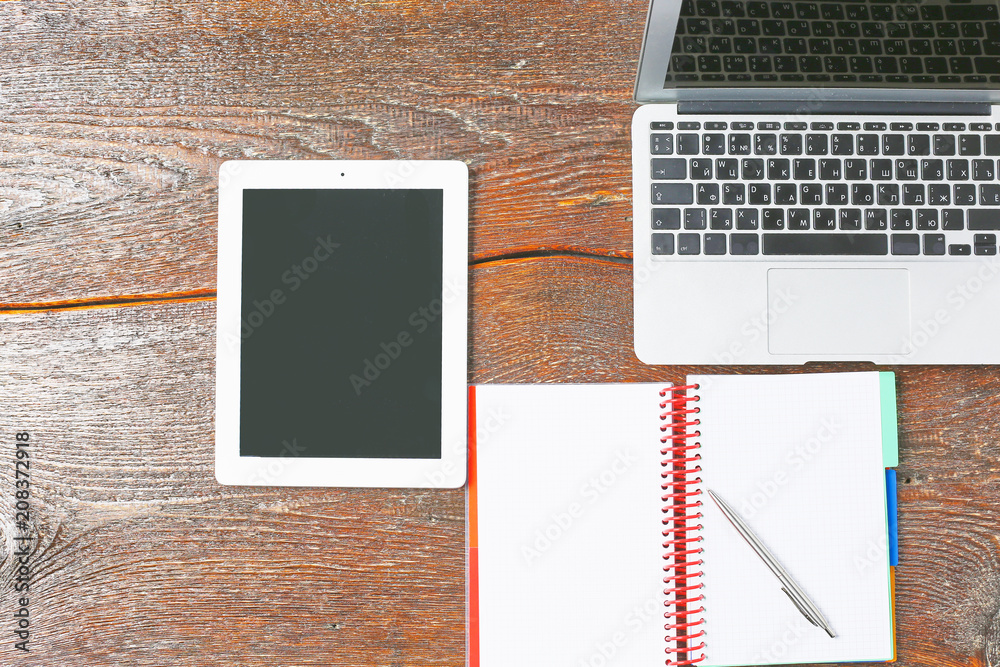 Laptop, tablet and notebook are on a wooden table