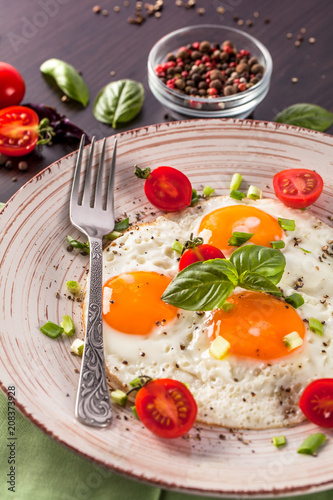 Concept of healthy eating. Protein for athletes. Tourist breakfast. Fried eggs lie on a handmade ceramic plate, fork, cherry tomatoes, basil. Black background. Copy space, top view. © zukamilov