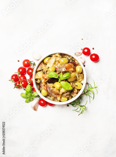 Stewed aubergines with vegetables and herbs in a bowl, light background, top view