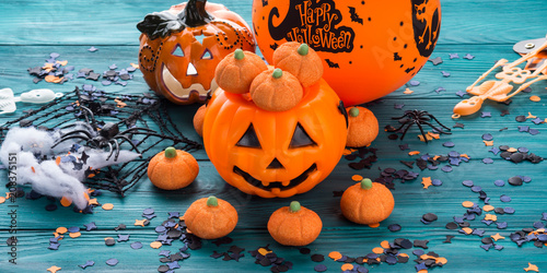Halloween trick or treat still life on dark green. Toy pumpkin, sweets, marshmalllow, confetti. Holiday mood background