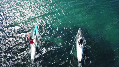 Aerial drone bird's eye view of 2 men exercising sport sup board in turquoise clear waters, Greece