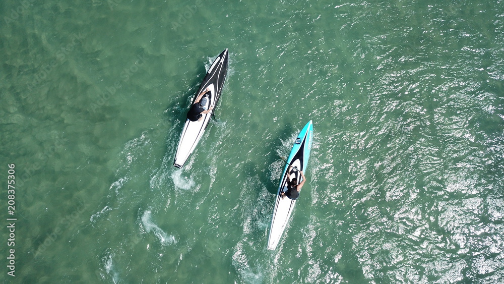 Aerial drone bird's eye view of 2 men exercising sport sup board in turquoise clear waters, Greece