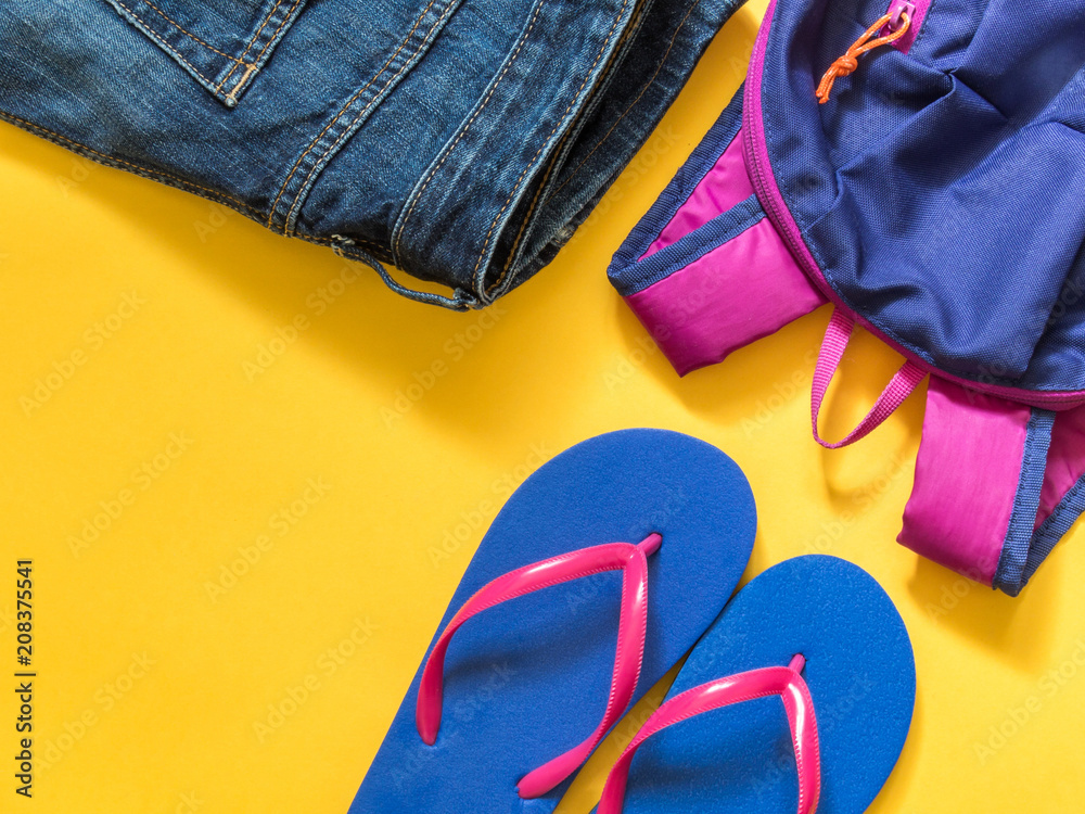 Travel vacation background. Flip flops, backpack, jeans on a yellow background. Flat lay