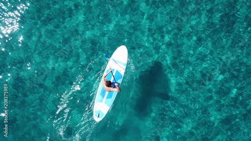 Aerial drone bird's eye view of a man exercising sup board in turquoise tropical clear waters at sunset