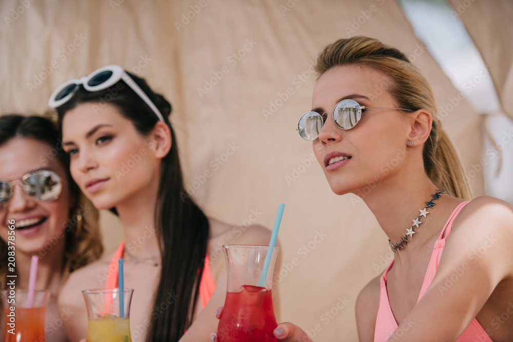 beautiful girls in swimwear and sunglasses drinking cocktails in bungalow on beach beautiful girls in swimwear and sunglasses drinking cocktails in bungalow on beach
