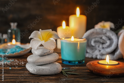 Spa stones with beautiful flower and burning candles on wooden table