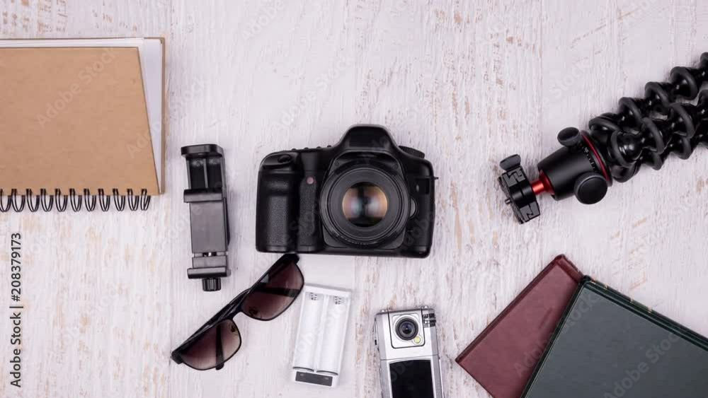 Stop motion animation of travel kit on wooden background. There are DSLR and action camera, books, charger and passport