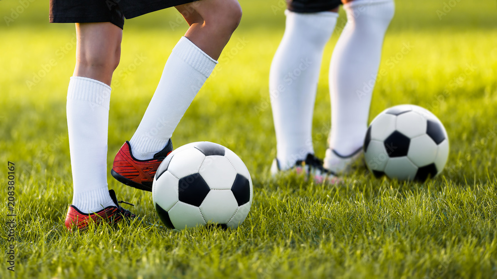 Two young football players training on a grass field. Boys in a sportswear. Players wearing white football socks and soccer boots. Football horizontal background