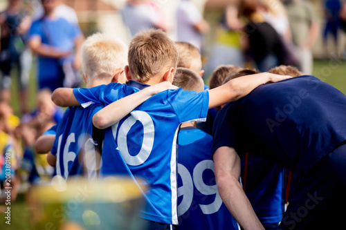 Young football players in blue jersey sportswear. Group photo with football coach. Young sports team with football coach. Pep talk with coach before the final match. Football school tournament