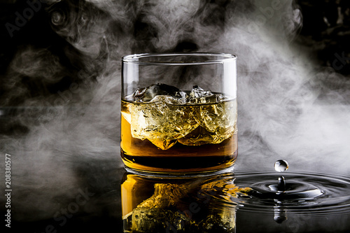 whiskey with ice on black background with splashes of water and smoke