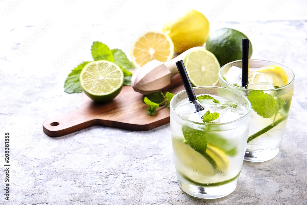 Fototapeta premium Two glasses of refreshing non alcoholic mojito lemonade drink with organic lemon, lime slices, mint leaves, straw, ice cubes on grunged grey concrete table background. Close up, top view, copy space.