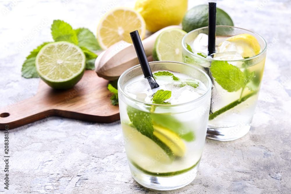 Fototapeta premium Two glasses of refreshing non alcoholic mojito lemonade drink with organic lemon, lime slices, mint leaves, straw, ice cubes on grunged grey concrete table background. Close up, top view, copy space.