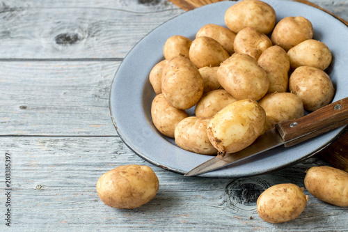 Young early potatoes in an old round bowl on a wooden table. 