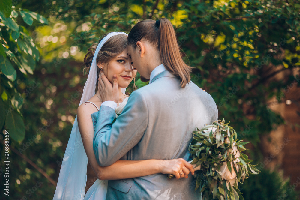 Fototapeta premium wedding couple. Beautiful bride and groom. Just merried. Close up. Happy bride and groom on their wedding hugging. Groom and Bride in a green garden. wedding dress. Bridal wedding bouquet of flowers