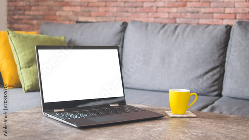 White screen laptop and a yellow cup on a table by a couch mock up