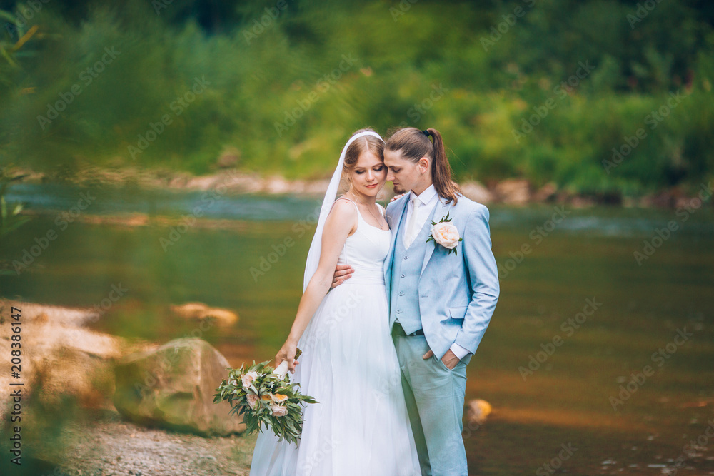 Sexy Couple in love kissing and hugging on the backdrop of fabulous mountains. Blue water mountains river. A woman and a man in a nice formal attire. Long light summer dress on a womans body. Wedding. Sexy Couple in love kissing and hugging on the backdrop of fabulous mountains. Blue water mountains river. A woman and a man in a nice formal attire. Long light summer dress on a womans body. Wedding.