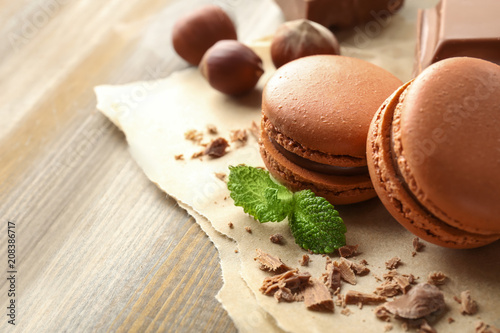 Tasty macarons, chocolate and hazelnuts on wooden background