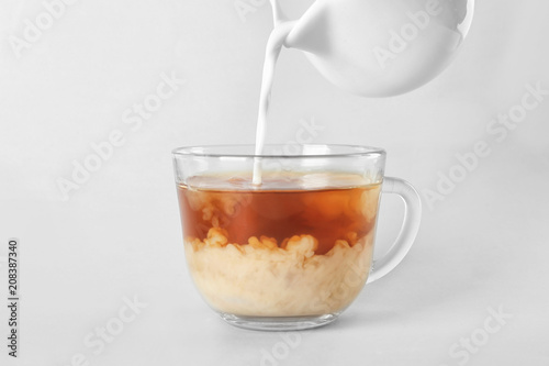 Adding milk to delicious tea on light background