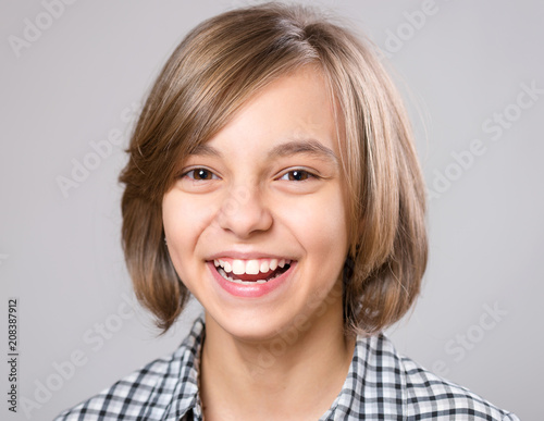 Beautiful caucasian teen girl on gray background. Schoolgirl smiling and looking at camera. Happy child - emotional portrait close-up.