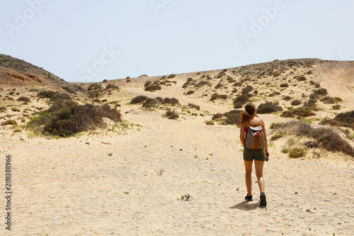 Lost in the desert. Young female hiker walking between desert dunes with uncertain step in Lanzarote, Canary Islands. 